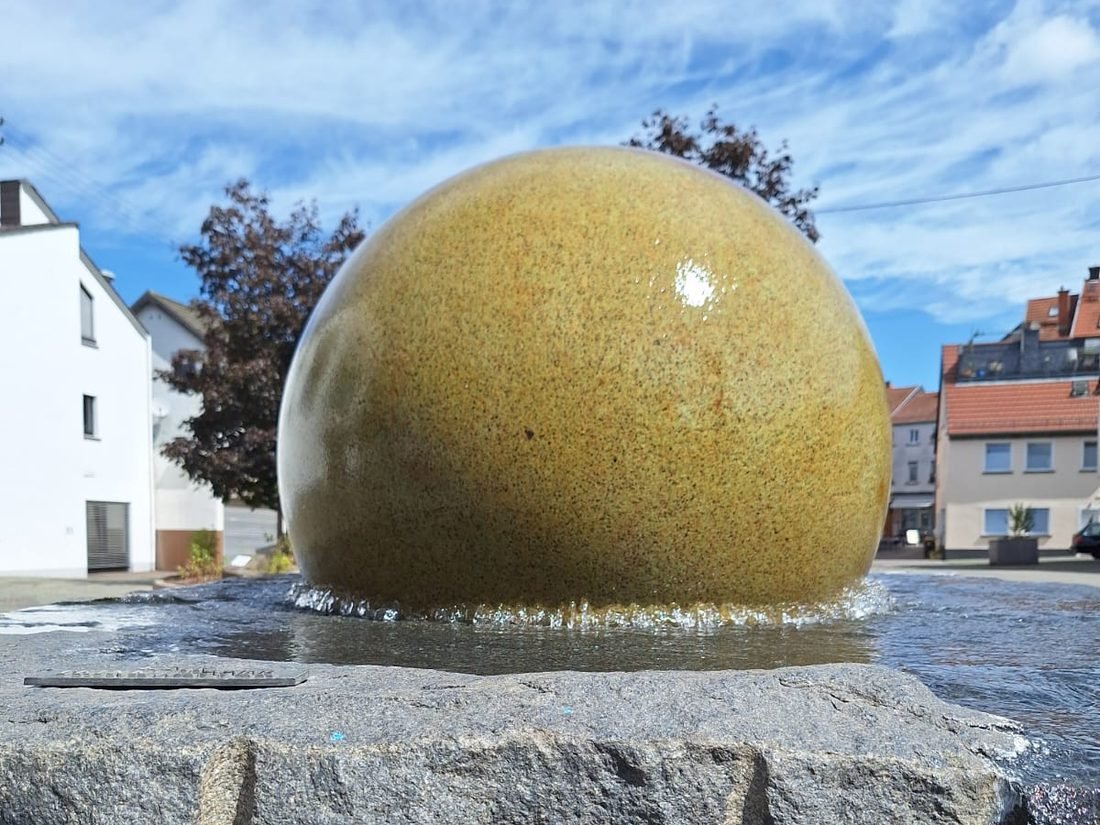 Der Kugelbrunnen in der Fußgängerzone von St. Wendel: eine große, gelblich glasierte Steinkugel, über die Wasser in ein flaches Becken läuft